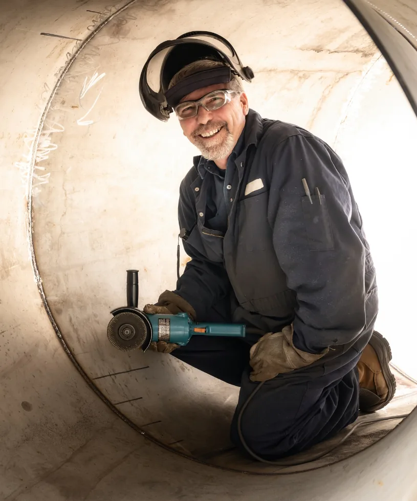 Smiling employee with a grinder inside a large fabricated steel cylinder