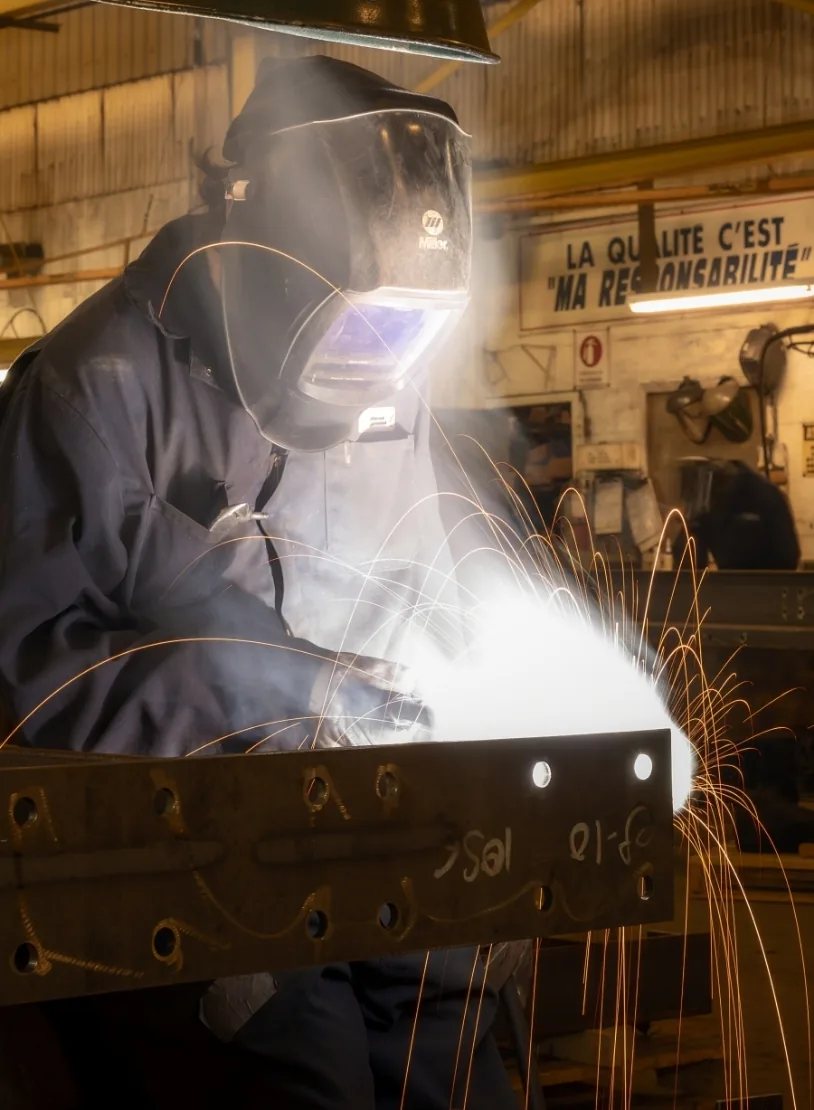 Soudeur au travail dans l’atelier, sous l’affiche « La qualité c’est ma responsabilité »